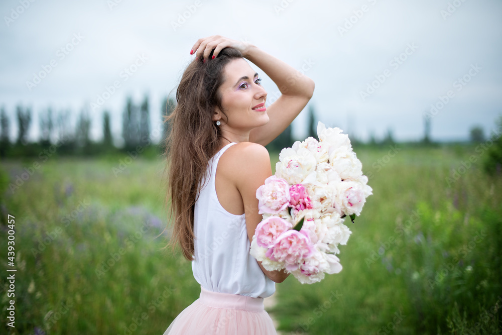 Beautiful girl with pink peonies, enjoying a bouquet of flowers on background of nature. Happy smiling woman in dress holds peonies in hands. Girl with a bouquet of flowers. Girl in wildflowers. Beautiful girl with pink peonies, enjoying a bouquet of flowers on background of nature. Happy smiling woman in dress holds peonies in hands. Girl with a bouquet of flowers. Girl in wildflowers.