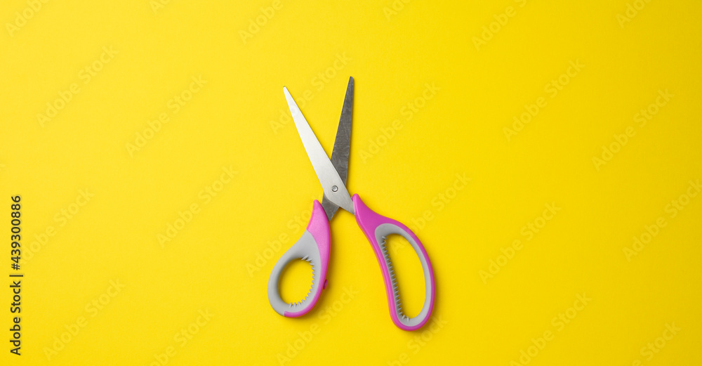 metal scissors with pink plastic handle on a yellow background metal scissors with pink plastic handle on a yellow background