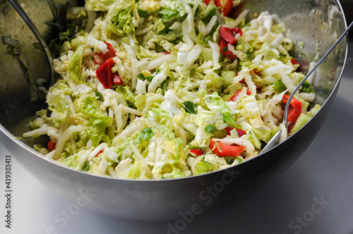 Salad of green Chinese cabbage, peppers and herbs in a silver bowl with spoons in it on a white background