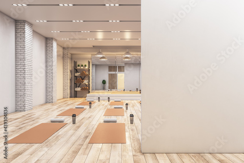 Bright concrete yoga gym interior with equipment, blank mockup space on wall, daylight and wooden flooring. Healthy lifestyle concept. Mock up, 3D Rendering.
