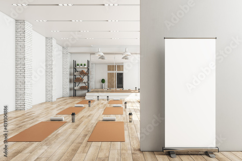 Modern concrete yoga gym interior with equipment, blank poster on wall, daylight and wooden flooring. Healthy lifestyle concept. Mock up, 3D Rendering.