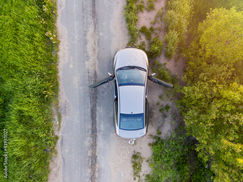 Car with open doors stands on side of rural road, aerial view