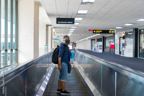 Senior Asian female traveler backpacker hipster boarded to plane on elevator arrived at international airport after get vaccinated coronavirus passport still wear face masks prevent COVID-19 disease