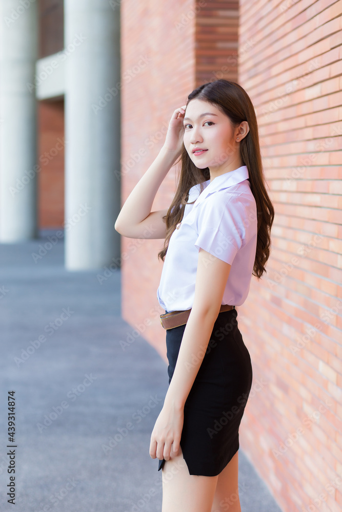 Portrait of an adult Thai student in university uniform. Asian beautiful girl is standing,relaxed, smiling and happily.