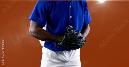 Mid section of african american male baseball pitcher against spot of light on orange background