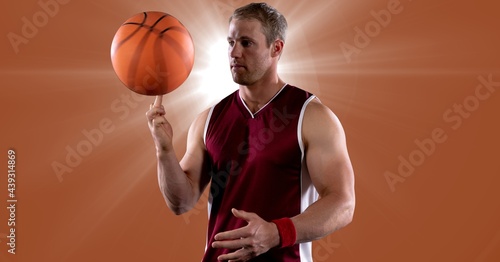 Caucasian male basketball player spinning basketball against spot of light on orange background