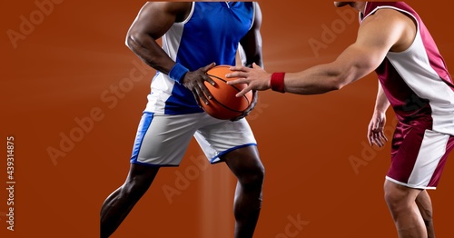 Mid section of two diverse male basketball players playing against spot of light in background