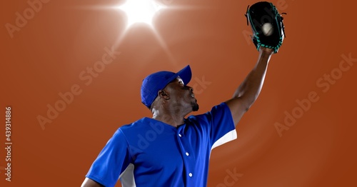 African american male baseball player catching a ball against spot of light in background