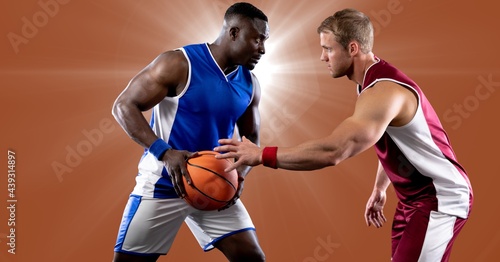 Two diverse male basketball players playing basketball against spot of light in background