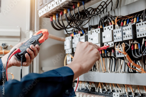 Electrician engineer uses a multimeter to test the electrical installation and power line current in an electrical system control cabinet.