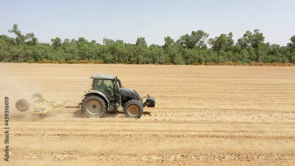 Tractor harvesting wheat in farmland out at the country. An agriculture aria drone view above green tractor combine machinery while processing wheat in piles of hay tubes Tractor harvesting wheat in farmland out at the country. An agriculture aria drone view above green tractor combine machinery while processing wheat in piles of hay tubes
