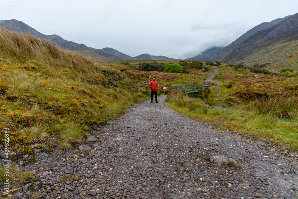 man wearing orange jacket standing in hilly landscape in mountains of Kerry Ireland