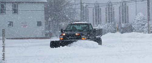 Valokuva Black truck with a snowplow clearing a parking lot behind buisnesses