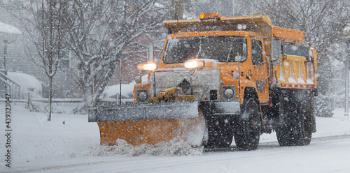 Yellow municipal snow plow plowing during a blizzrd photo