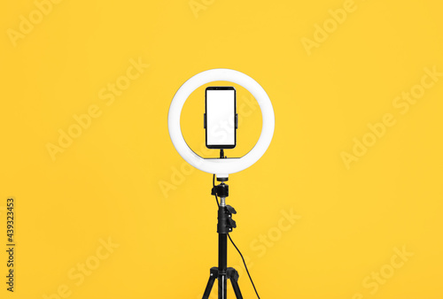 Modern tripod with ring light and smartphone on yellow background photo