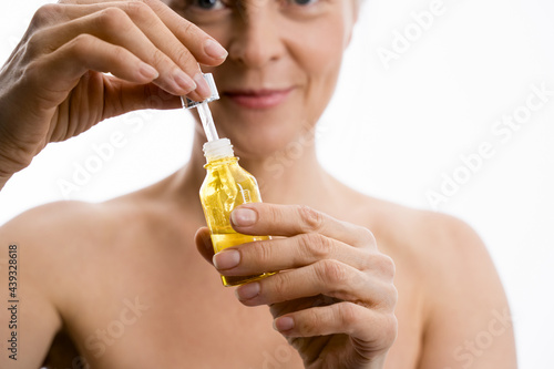 Senior lady holding bottle and receiving serum oil treatment at her face