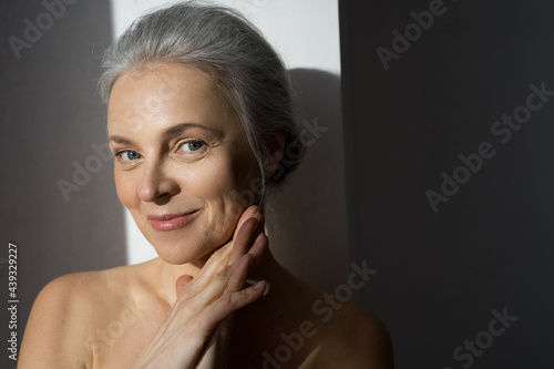 Aged woman with healthy glowing skin and toothy smile touching face gently photo