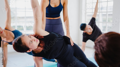 Young Asian sporty attractive people practicing yoga lesson with instructor. Asia group of women exercising healthy lifestyle in fitness studio. Sport activity, gymnastics or ballet dancing class.