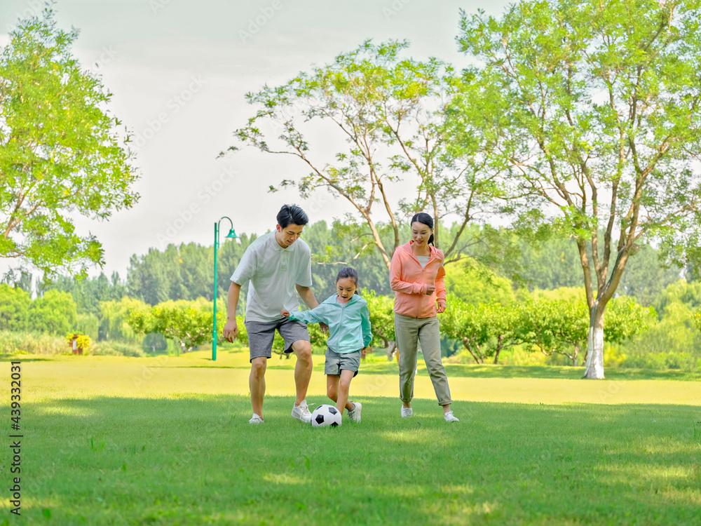 Happy family of three playing football in the park