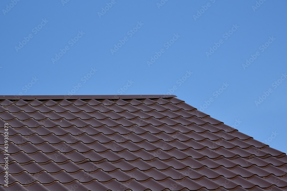 Close up of brown steel roof. Dark steel tiled roof background, Europe. View of a new house. Construction of a new residential private house on blue sky background. pattern Close up of brown steel roof. Dark steel tiled roof background, Europe. View of a new house. Construction of a new residential private house on blue sky background. pattern