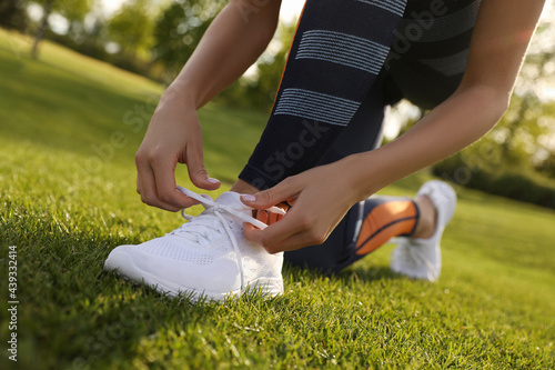 Woman tying laces of sneakers outdoors, closeup. Morning fitness