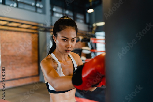Young Asia lady kickboxing exercise workout punching bag tough female fighter practice boxing in gym fitness class. Sportswoman recreational activity, functional training, healthy lifestyle concept. © tirachard