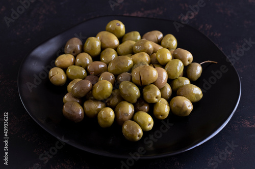 Green olives on a dark background. Tasty green olives in the plate.