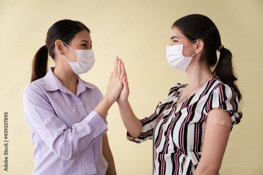 Invitation to vaccinate with covid 19. 2 women wearing masks facing each other and touching hands, showing arms with plaster to cover the wound. Concept of preventing the spread of coronavirus.