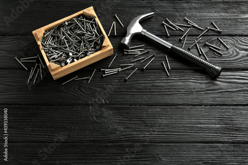 Hammer and metal nails on black wooden table, flat lay. Space for text