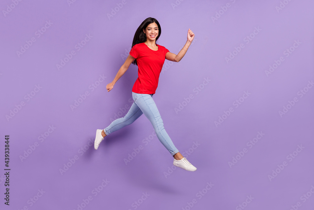 Full length photo of adorable pretty woman dressed red t-shirt jumping high running fast smiling isolated purple color background