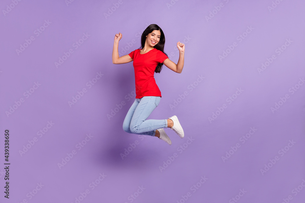 Full length photo of pretty lucky young lady wear red outfit smiling jumping high rising fists isolated violet color background
