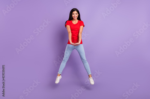 Full length photo of charming sweet woman dressed red t-shirt jumping high smiling isolated purple color background
