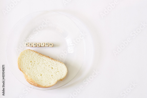 Piece of bread in a transparent plate next to the inscription pension. Minimum pension and old age poverty concept. Blank copy space for inscription