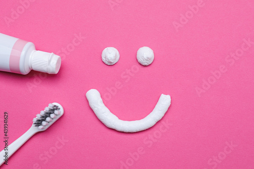 Funny face made with toothpaste, brush and tube on pink background, flat lay