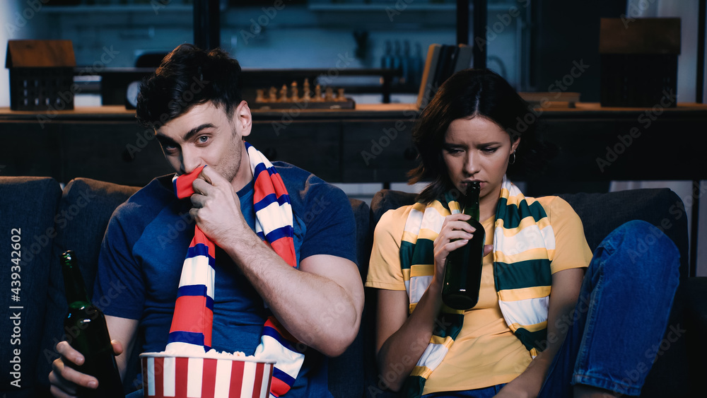 man covering mouth with scarf while watching championship with upset woman. man covering mouth with scarf while watching championship with upset woman.