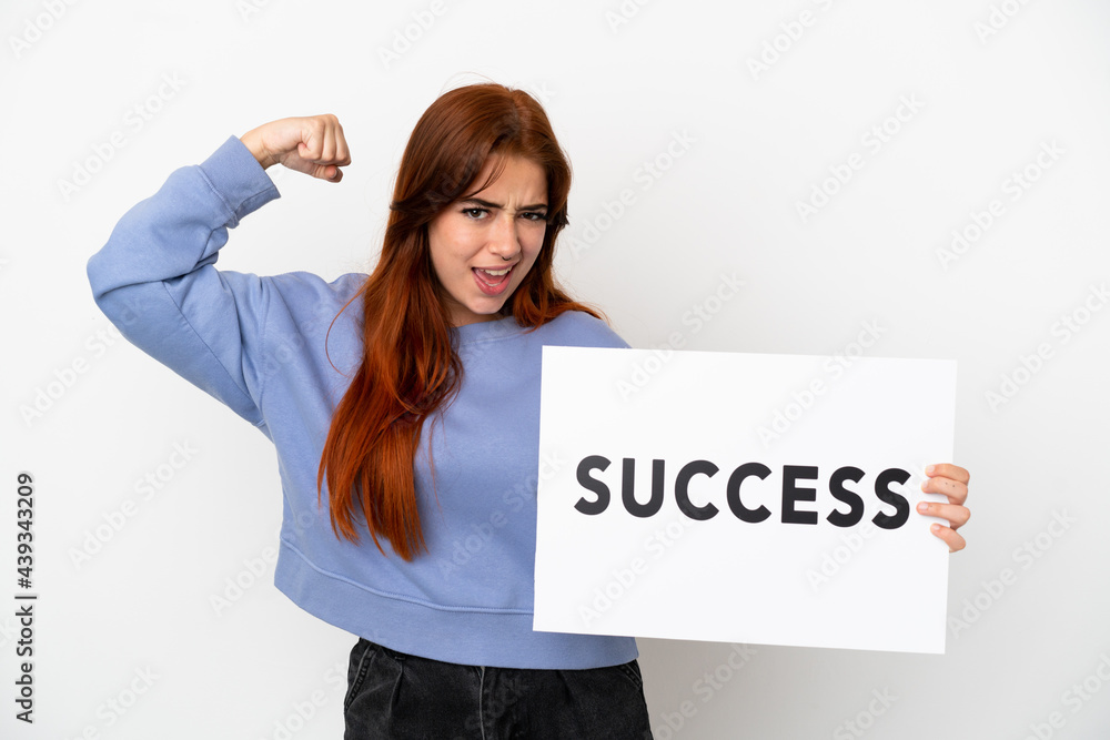 Young redhead woman isolated on white background holding a placard with text SUCCESS and doing strong gesture Young redhead woman isolated on white background holding a placard with text SUCCESS and doing strong gesture