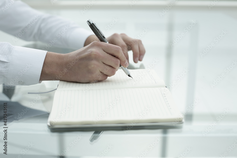 Office worker's hand writes in notebook in office Office worker's hand writes in notebook in office