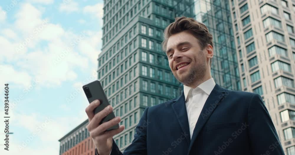 Handsome Bearded Businessman Browsing Smartphone, Chatting on Social Media. Confident Male wears Elegant Suit. Standing in front of Huge Company Building. Chatting with Colleagues. Applications.