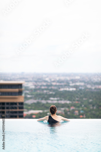Relaxing at swimming pool on rooftop, Woman enjoying the view with arms raised from swimming pool