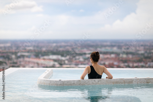Relaxing at swimming pool on rooftop  Woman enjoying the view with arms raised from swimming pool