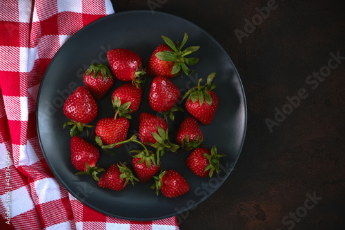 Ripe red strawberries in a black plate with napkin