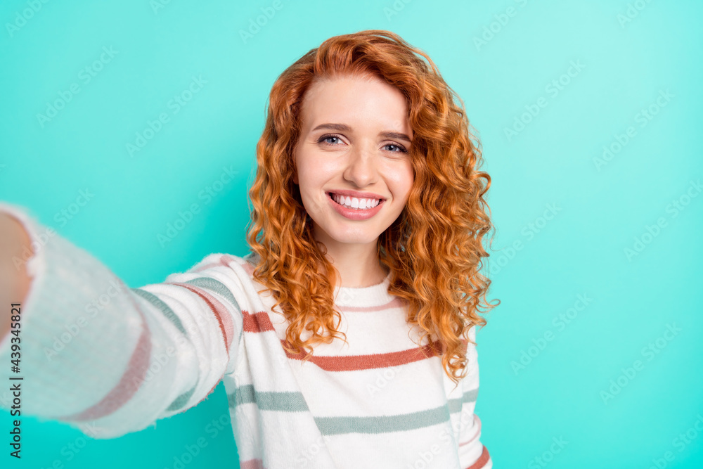 Photo portrait of red haired girl in striped sweater smiling taking selfie isolated vibrant turquoise color background Photo portrait of red haired girl in striped sweater smiling taking selfie isolated vibrant turquoise color background
