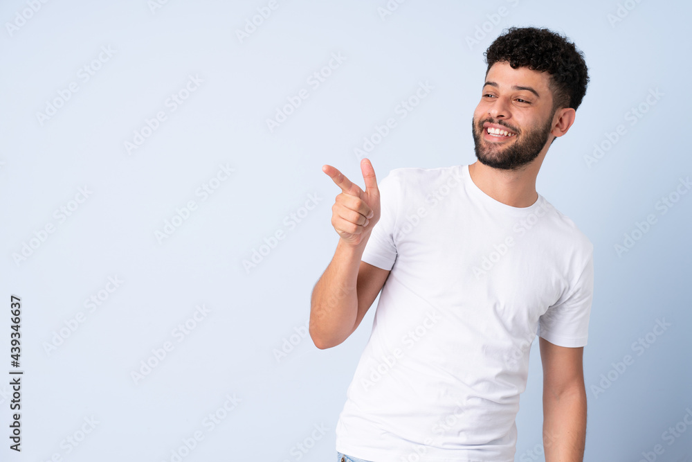 Young Moroccan man isolated on blue background pointing finger to the side and presenting a product Young Moroccan man isolated on blue background pointing finger to the side and presenting a product