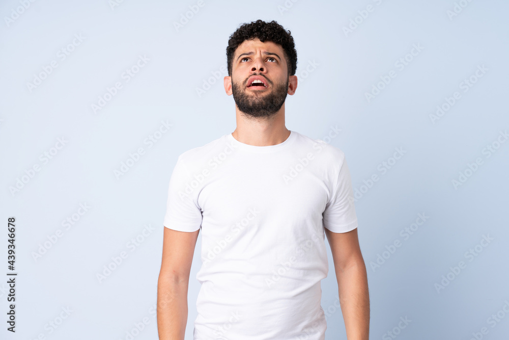 Young Moroccan man isolated on blue background looking up and with surprised expression Young Moroccan man isolated on blue background looking up and with surprised expression