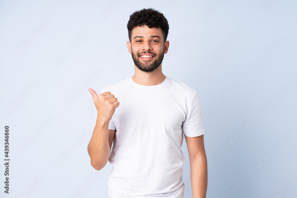 Young Moroccan man isolated on blue background pointing to the side to present a product Young Moroccan man isolated on blue background pointing to the side to present a product