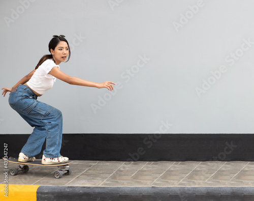 Asian young woman playing surfskate or skate board isolated on gray background at urban city outdoor. Extream sports photo