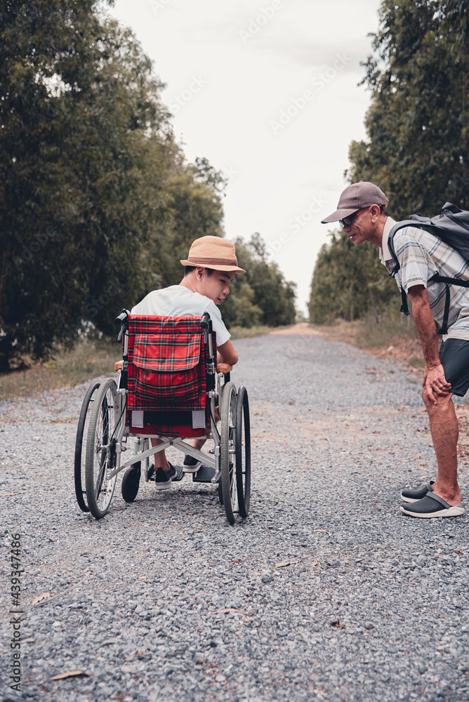 Naklejka premium Disabled child sitting on wheel​chair​ and father have fun with activity on the outdoor park on travel, Lifestyle in education age of disabled children, Happy disability kid concept.