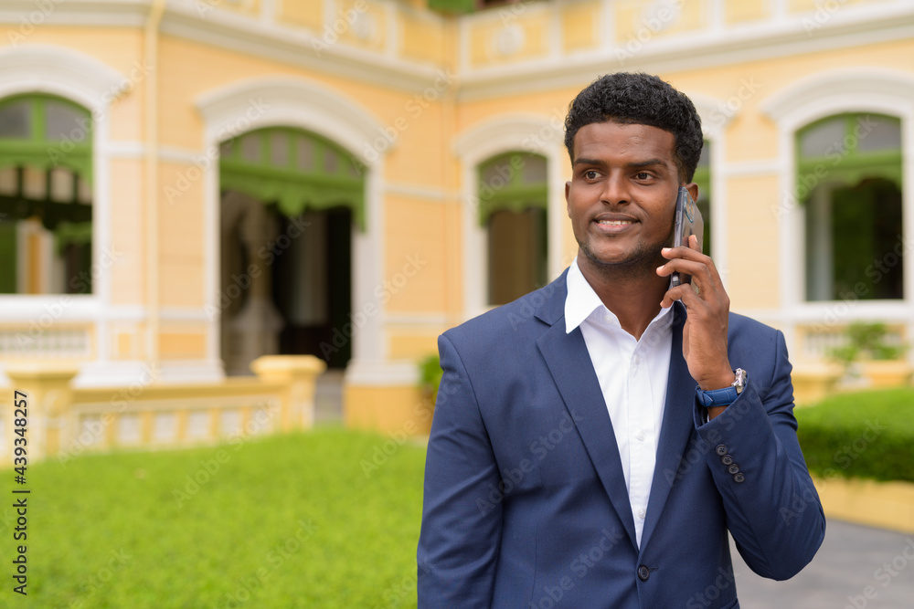 Happy African businessman outdoors wearing suit and talking on mobile phone while smiling Happy African businessman outdoors wearing suit and talking on mobile phone while smiling