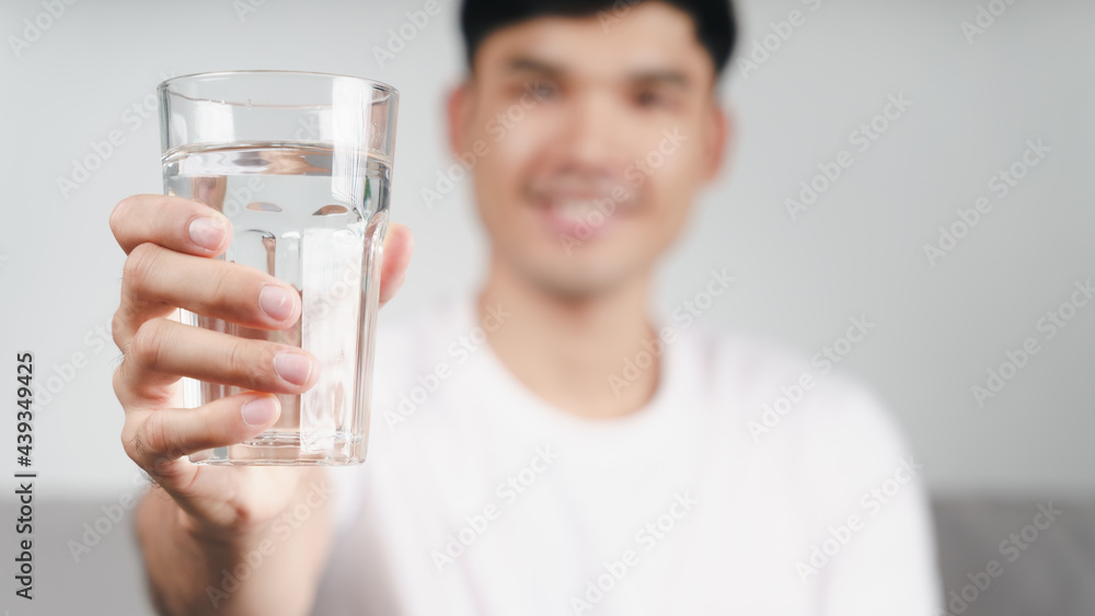 handsome asian man drinking a glass of water on the sofa at living room . handsome asian man drinking a glass of water on the sofa at living room .