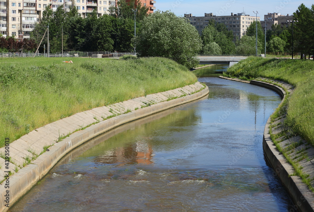 Narrow winding river with grass-covered banks in the city, Okkervil River, Rosiysky Prospekt, Saint Petersburg, Russia, June 2021